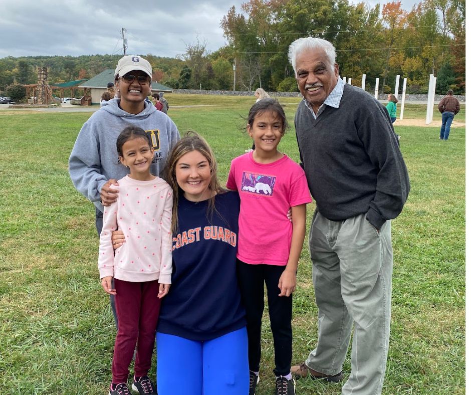 Group of five diverse individuals, including a young woman in a Coast Guard sweatshirt, smiling with three children and an elderly man, set in a grassy outdoor area, reflecting community and support themes relevant to caregivers and families impacted by Type 1 Diabetes.